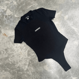 Black t-shirt short sleeve bodysuit with ‘SUPERIOR’ logo on a grey concrete surface for flatlay product shot 