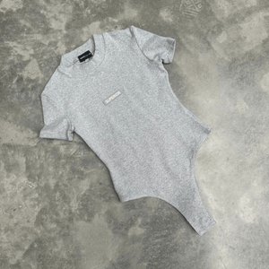 Grey t-shirt bodysuit with a small logo on a textured grey surface for flatlay